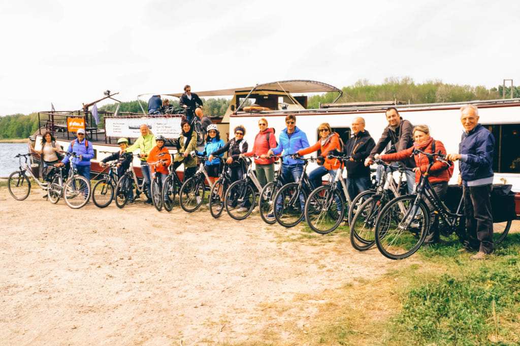 Gruppo di ciclisti in posa lungo un canale olandese con barca sullo sfondo, vacanze in bici e barca "Girolibero" in Olanda